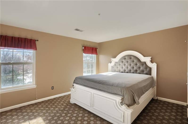 Two vivid windows cast beautiful natural lighting into the primary bedroom and shine on the custom carpeting.