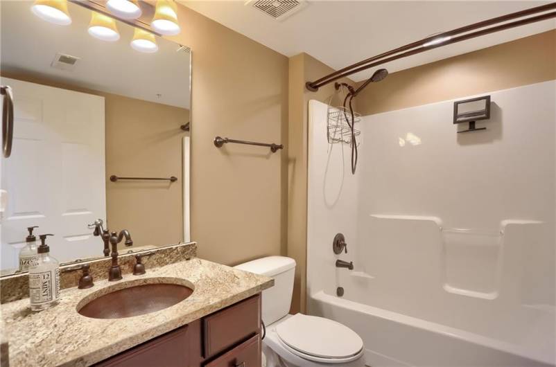 The shared hall bathroom has a granite topped vanity with a hammered, copper sink and a tub/shower combo.