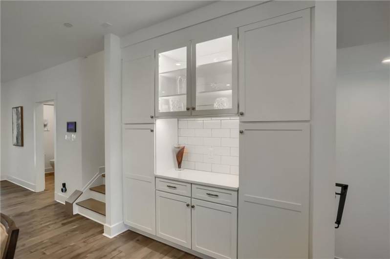 The custom coffee bar area features showcase cabinets, under cabinet lighting and soaring storage.