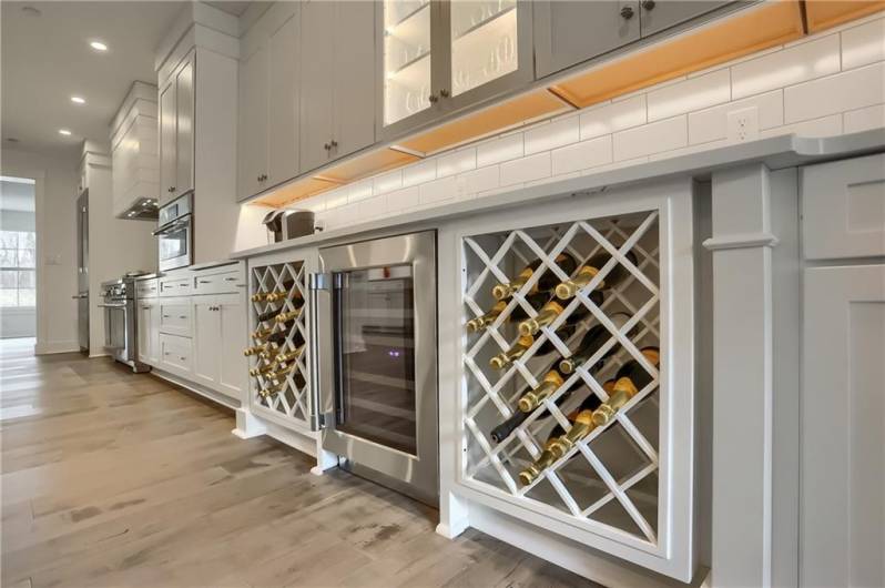 A beverage cooler is flanked with built in wine racks.