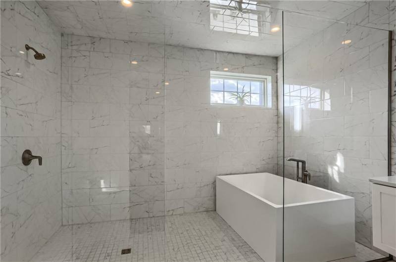 The wet room enclosed in glass features gorgeous tile and a luminous window.