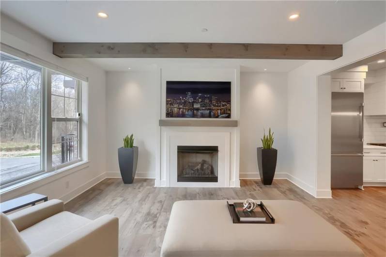 Sleek family room features a fireplace, exposed beams, gorgeous sprawling hardwood flooring and a large picture window.