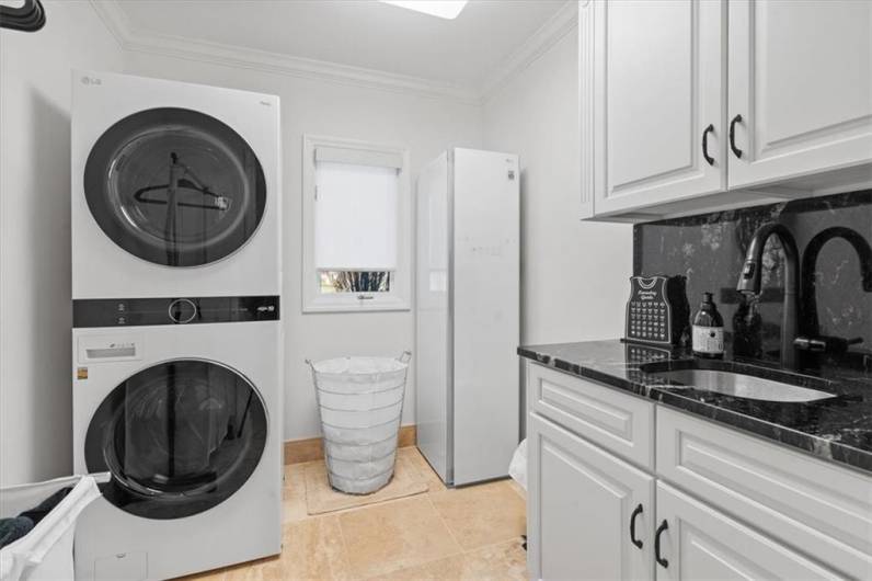 First floor laundry room with built-in cabinetry with granite counter-top, washer, dryer and steamer