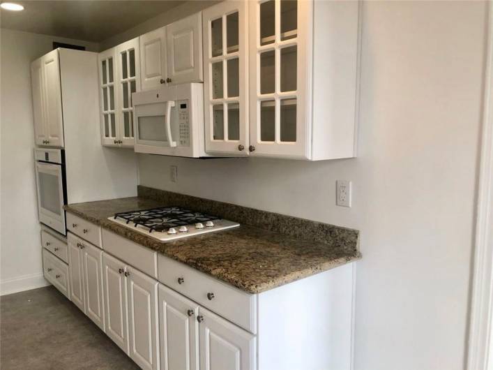 White gas stove top and oven, refrigerator, dishwasher, and microwave. Granite countertops. Neutral floors.