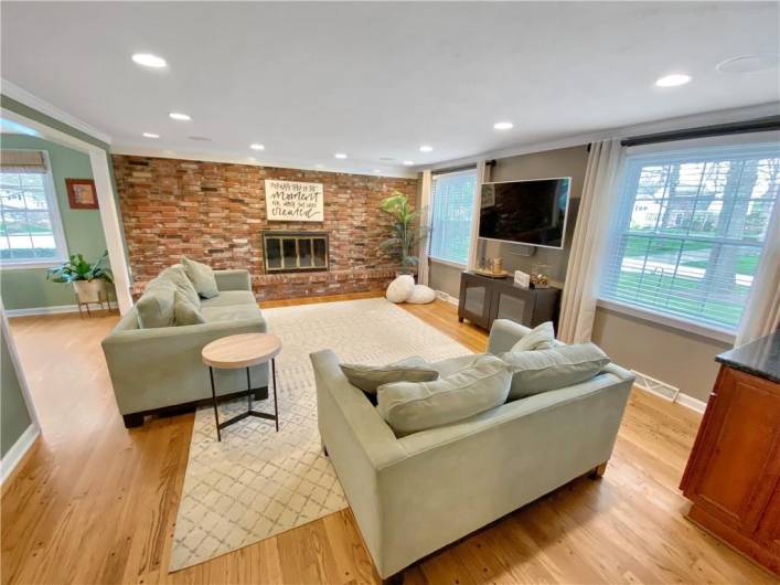 A first floor family room features pegged wood floors, recessed lighting, and a brick fireplace.