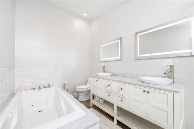 Primary Bathroom is luxurious w/ jet tub, lighted mirrors, vaulted ceiling and glass surround shower
