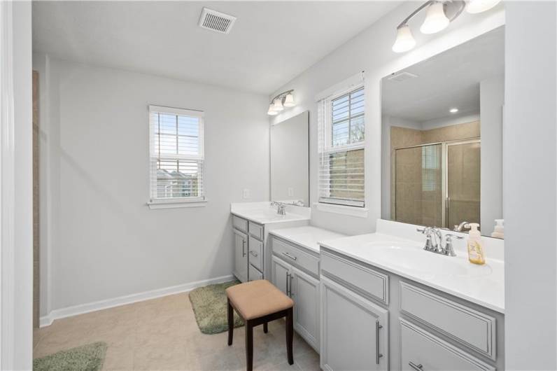 Double vanity with stone tops, additional cabinetry, tile floors and a linen closet.