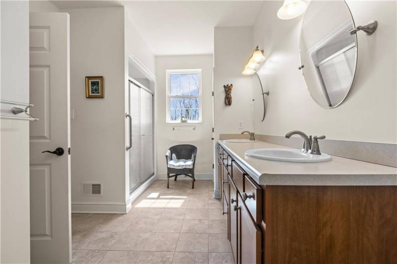 Double vanity with wood cabinetry, walk-in shower and linen closet for additional storage.