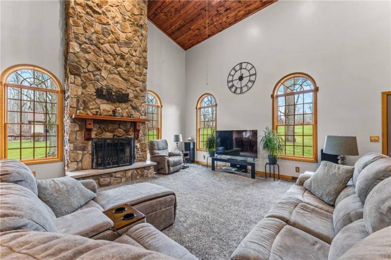 Vaulted great room with large windows overlooking the property and a wood burning fireplace.