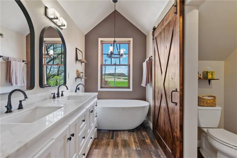 The luxurious master bath features a tiled walk-in shower (not shown here), a lush soaking tub, and a double bowl granite vanity.  The barn door separates the toilet room from the main bath.