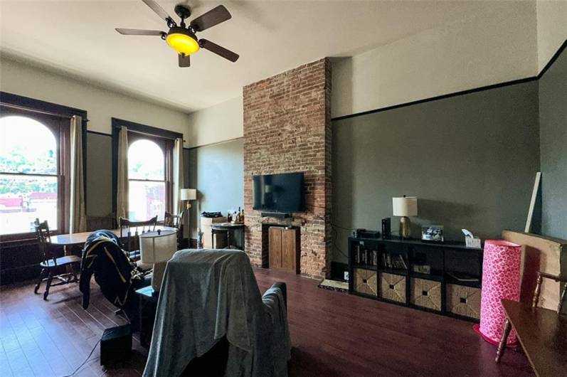 d floor apartment living room with exposed brick decorative fireplace, hardwood floors, large bright windows facing E Carson St and soaring 12 foot ceilings.