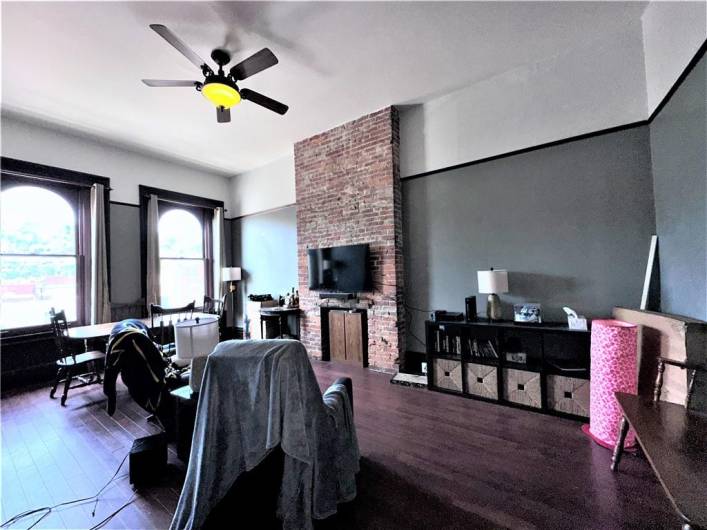 3rd floor apartment living room with exposed brick decorative fireplace, hardwood floors, large bright windows facing E Carson St and soaring 12 foot ceilings.