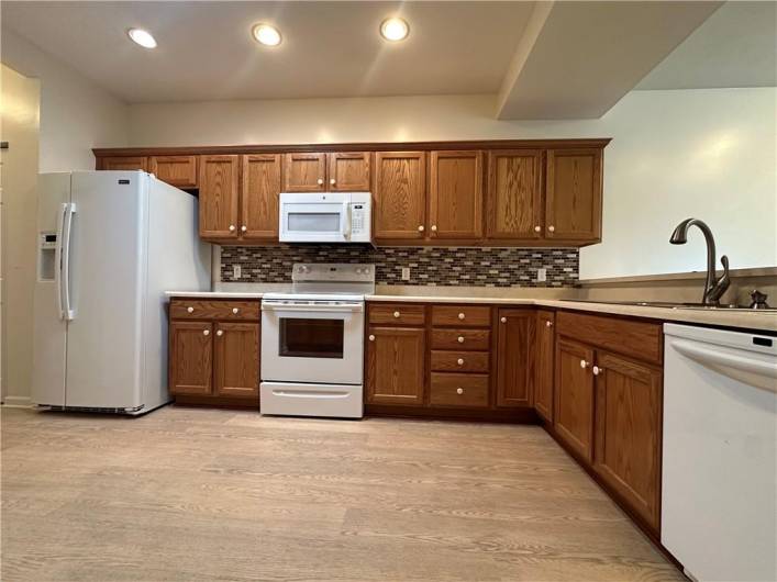 Oak cabinetry with ceramic backsplash, new LVT floor, white appliances (including electric range, microwave and dishwasher), stainless steel sink, pantry, recessed lights.