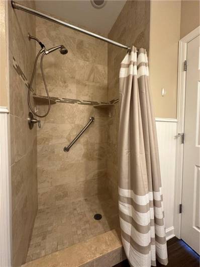 Ceramic shower with handheld shower faucet and grab bar.