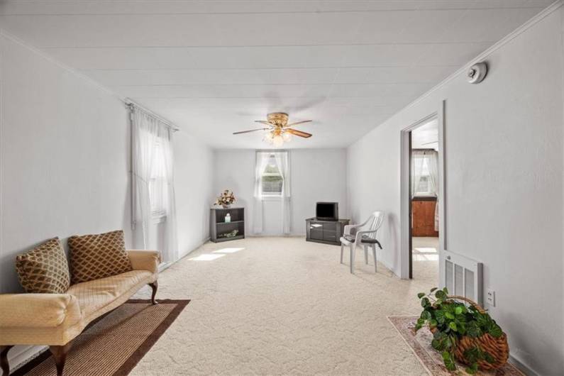 2nd floor apartment living room is 18x11'. It features 2 windows & a ceiling fan. The door on right leads to a bedroom. There is hardwood flooring under this carpet.