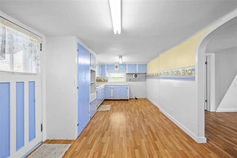 View of the kitchen from bedroom of the small house. The main entry door is to the left. The entrance to the living room is to the right. New vinyl flooring has just been installed.