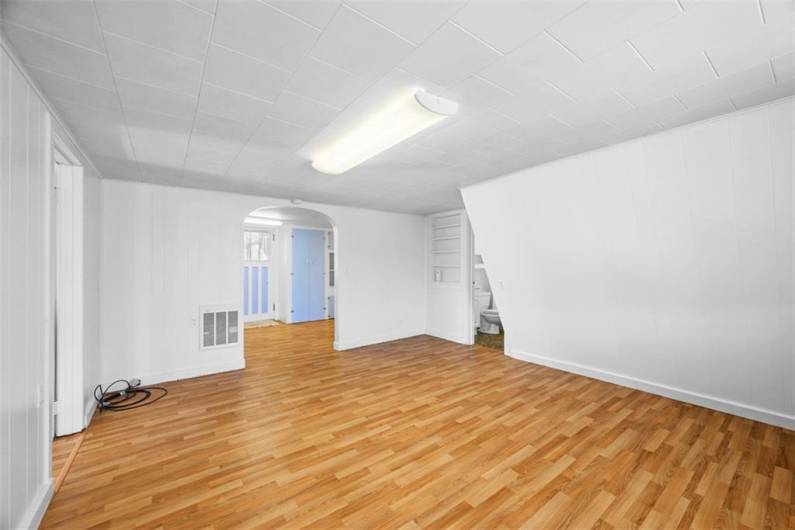 View of the living room of the small house from the far wall, looking toward the kitchen. The bathroom can be seen to the right. New vinyl flooring has just been installed.