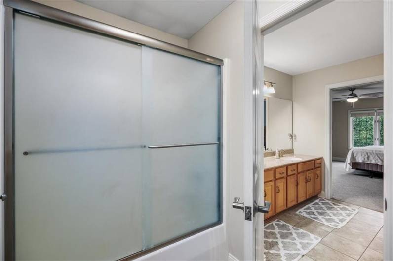 Ensuite/ hall bath with glass shower doors and tile flooring.