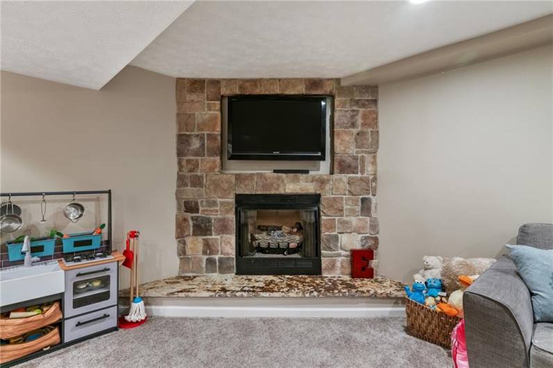 Game room features gas log stone fireplace with marble hearth.