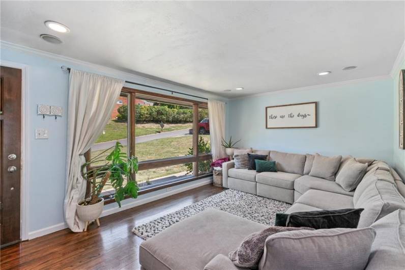 Sun drenched living room boasts large picture window, recessed lighting and crown molding.