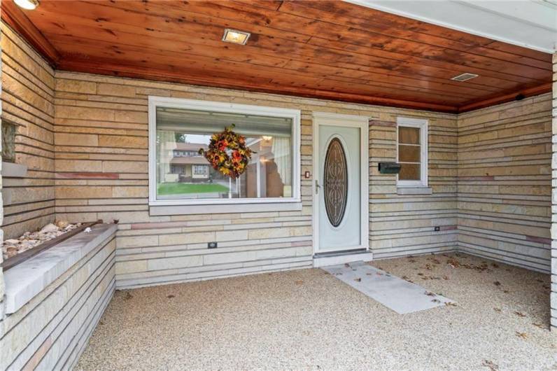 Front 19x8 Covered Porch Highlighted by Knotty Pine Wood Ceiling, Pebblestone Flooring, Glass Block Window & Stone Planter Ledge Welcoming into Main Front Entry through Lead Glass Oval Door