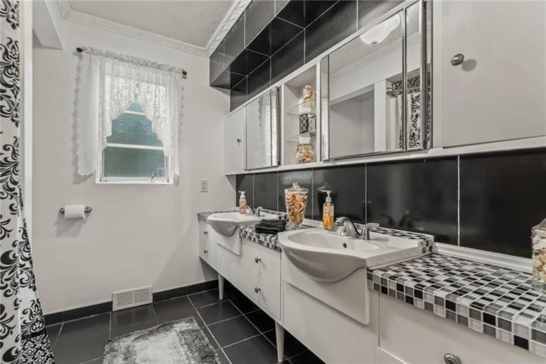 Elegant Main Full Bathroom housing a Double Sink Vanity, Mosaic Tile Countertop, Plenty of Cabinets & Storage areas highlighted w/ Carrera Glass Backsplash, trimmed by detailed Crown Molding, Ceramic Tile Flooring & Updated Deep Tub Surround