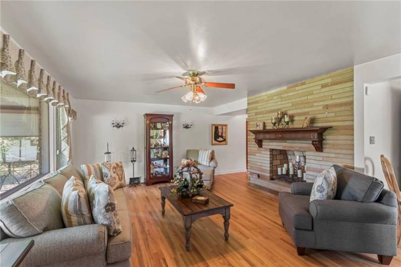 Large Living Room w/ Majestic Stone Fireplace taking Center Stage, flanked by Exquisite Antique Wall Sconces, Huge Picture Window allows plenty of Natural Light while offering Stunning Views of Nature's Beauty overlooking Vast Sprawling Backyard