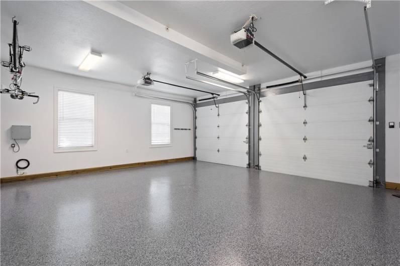 A pristine garage featuring large windows a 220 outlet and exceptional flooring. The garage doors are oversized to accommodate large vehicles.