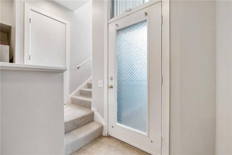 View of the front door, stairway, and kitchen pantry from the interior first floor 'hallway' en route to the oversized sunken living room.