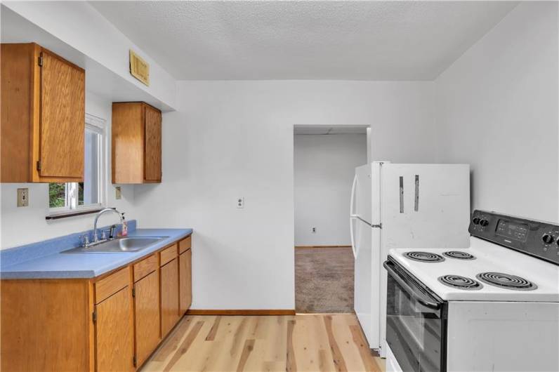 Another view of the kitchen with stainless sink, window above, refrigerator and stove (as is condition).