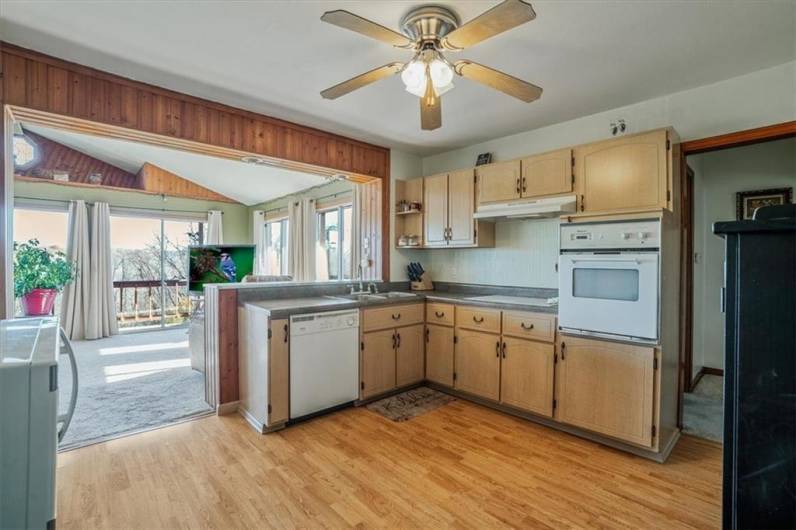 Functional kitchen with ample cabinetry, built-in appliances, and a large pass-through window that opens to a bright sunroom with scenic views.