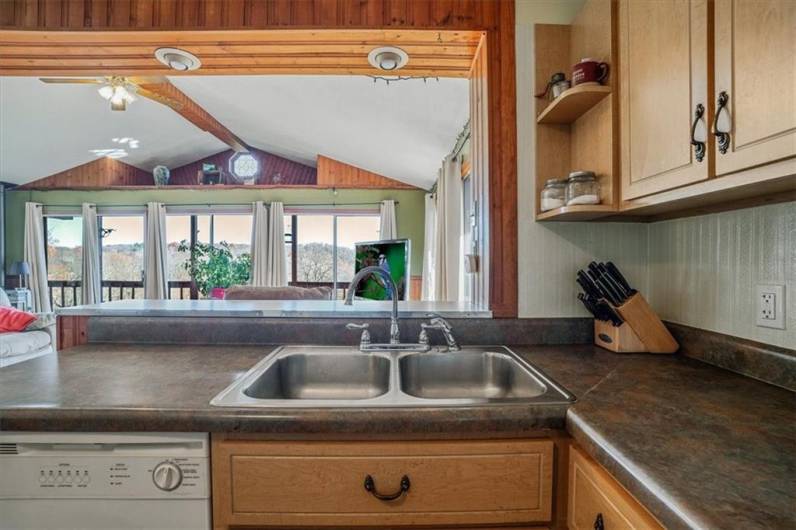 Double sink with a scenic view through the open pass-through window, connecting the kitchen to a sunroom with large windows that let in natural light and provide views of the surrounding landscape.