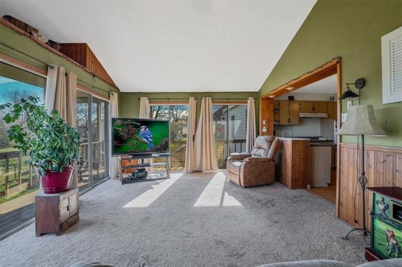 Sunroom with large windows and access to the deck, offering abundant sunlight and seamless indoor-outdoor living with serene views.