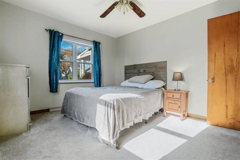 Bright and cozy bedroom featuring a neutral palette, large window for natural light, and ceiling fan, creating a peaceful and inviting space for relaxation.