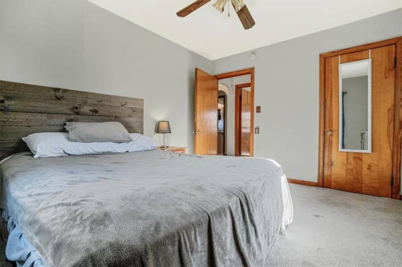 Spacious guest bedroom with a modern, rustic headboard, ceiling fan, and ample closet space. The neutral walls and wood accents provide a warm, inviting feel.