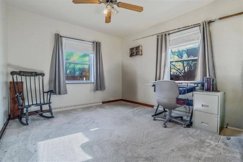 Versatile bedroom currently set up as a home office, featuring large windows that bring in plenty of natural light, neutral walls, and ceiling fan. A perfect space for work or study, with the potential to be easily converted back to a bedroom.