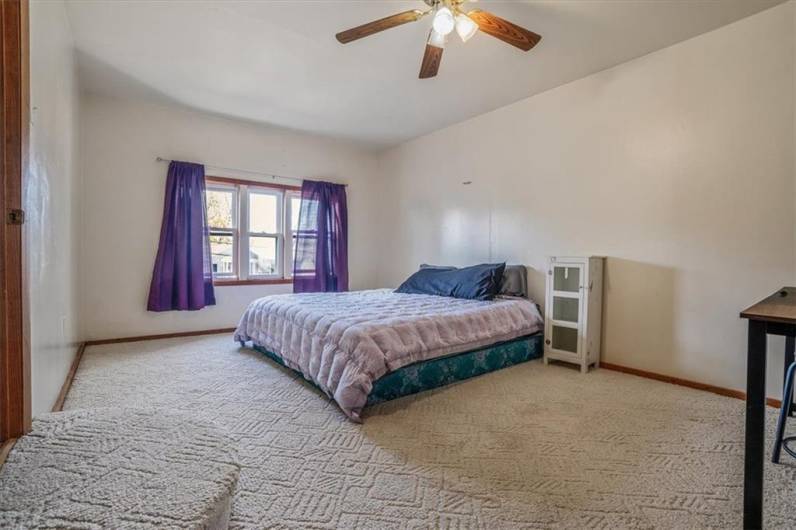 This inviting bedroom (upstairs) is filled with natural light from a large window. Neutral tones and a ceiling fan add comfort and warmth, making it a perfect retreat at the end of the day.