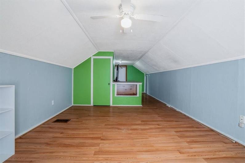 An extended loft area with colorful walls and versatile space, perfect for a playroom, home office, or creative studio. Includes built-in shelving and ample floor space.