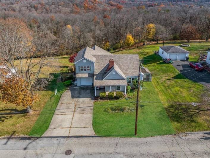 A welcoming front view of the home with a neatly kept lawn, attached garage, and inviting front porch, surrounded by natural beauty.