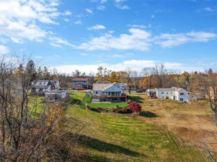 This wide-angle shot from a slight distance showcases the home’s rear elevation, emphasizing the deck, backyard, and surrounding open space. It provides a sense of the property’s expanse and layout relative to the surrounding area.