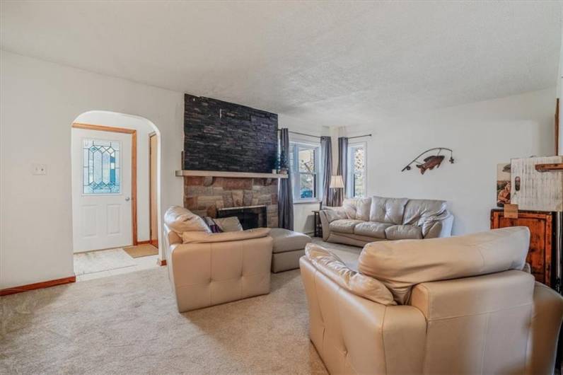 Cozy living room with soft carpeting, a striking stone fireplace with a wood mantle, and abundant natural light for a relaxing atmosphere.