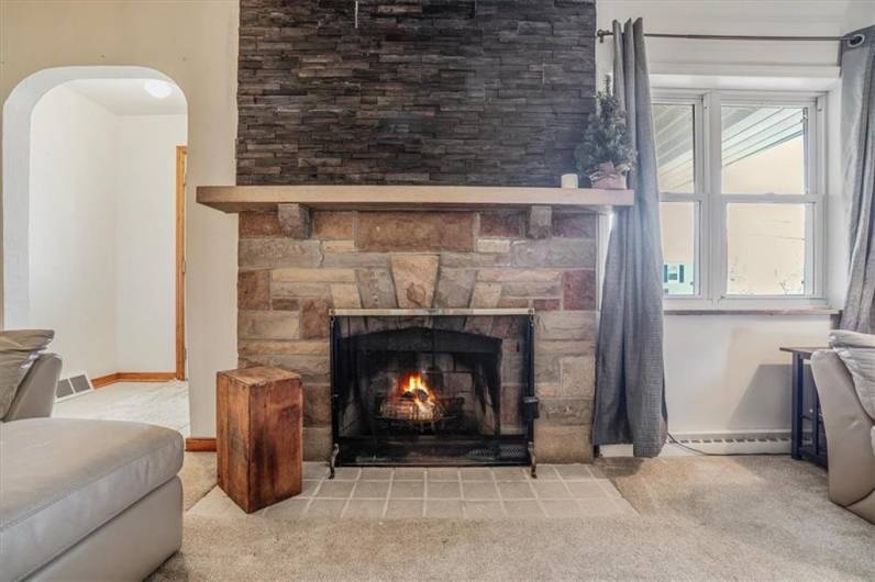 Elegant lounge area with a stone-accented fireplace, perfect for gatherings. Large windows provide natural light and views of the front yard.