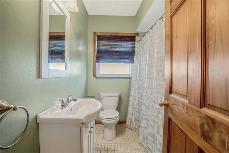 Charming bathroom with a fresh, clean look, featuring a single vanity, tiled flooring, and a large window for natural light.