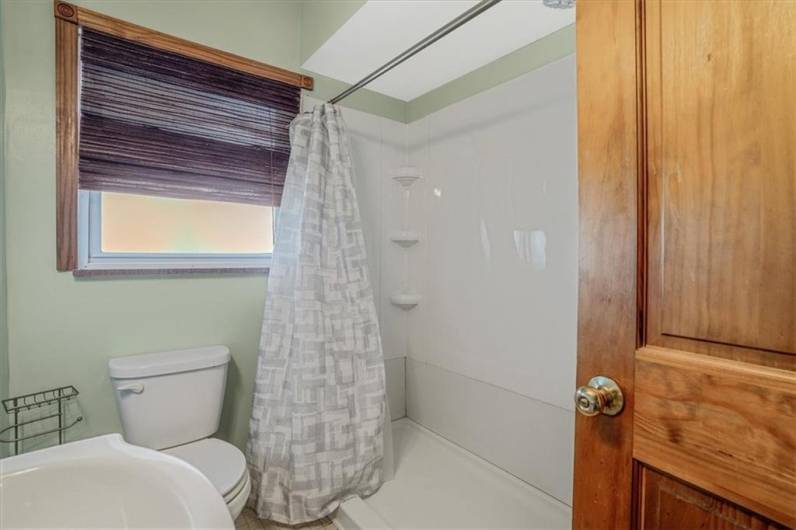 Spacious shower area with a modern curtain and functional shelving, offering convenience and style in this well-lit bathroom.