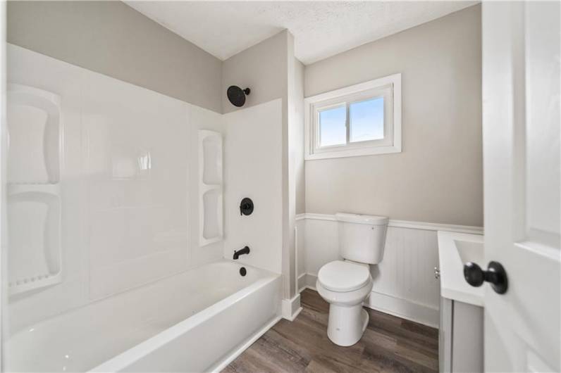 Brand new full bath with updated matte black fixtures, warm tone laminate flooring, & more!