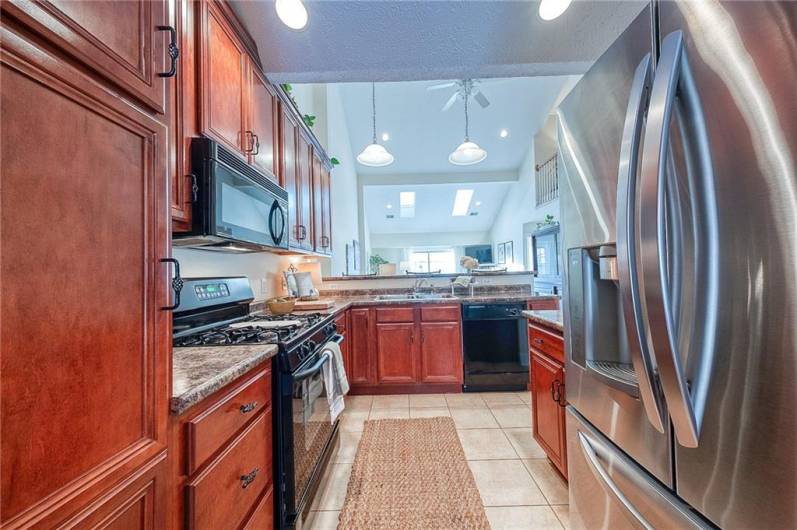 The kitchen boasts solid wood cabinetry, tile flooring, gas range, and high-top seating