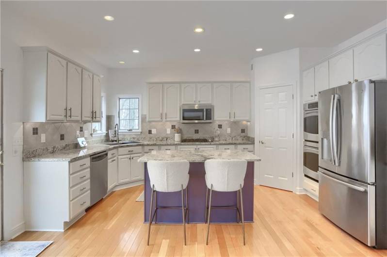 A gorgeous chef's kitchen features modern white cabinetry with a blue island, featuring ample granite counter space.