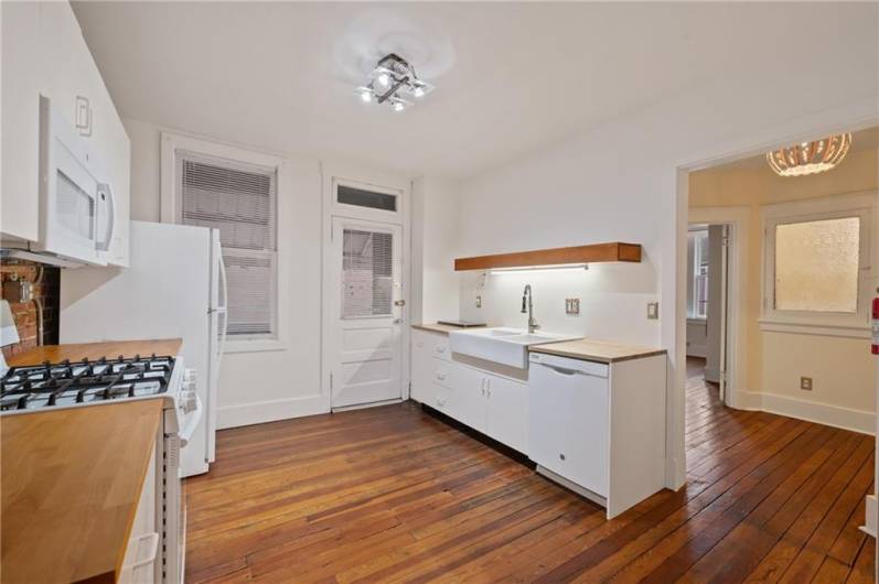 Farmhouse sink, dishwasher, gas stove, microwave, and fridge. Well equipped! Contemporary light fixtures are visible in the kitchen as well as the foyer. Notice the refinished hard wood floors.