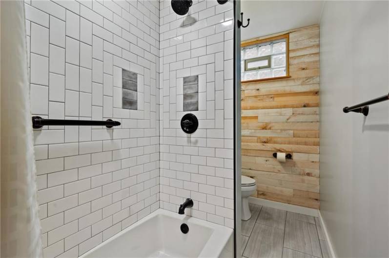 Cool and modern remodeled bathroom. Tiled tub/shower, wood wall, and newer flooring. Note the glass block window for privacy also features a vent which is great in a bathroom.