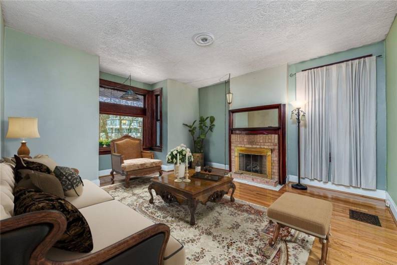 This inviting living room exudes warmth and character, featuring a stunning decorative fireplace that serves as a charming focal point. A gorgeous leaded window fills the space with natural light, casting intricate patterns that enhance the room’s timeless elegance. With its blend of classic details and cozy ambiance, this space is perfect for relaxing, entertaining, or simply enjoying the beauty of its architectural charm.